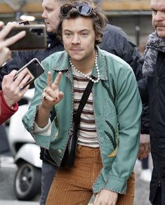 a man in a green jacket and brown pants is making the peace sign with his hand