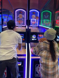 two people standing in front of an arcade machine with basketball hoops on the wall