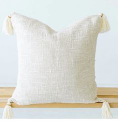 a white pillow sitting on top of a wooden bench with tasselled trims