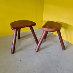 two wooden stools sitting next to each other in front of a bright yellow wall