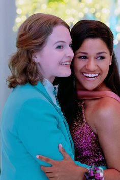 two women hugging each other in front of a christmas tree with lights on the background