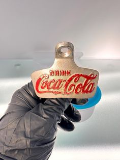 a gloved hand holding a bottle opener with the word drink coca cola on it