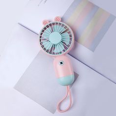 a pink and blue mini fan sitting on top of a piece of paper next to an envelope