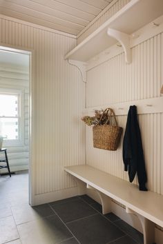 a white bench sitting under a window next to a basket on top of a shelf