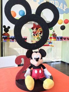 a mickey mouse sitting on top of a table in front of a happy birthday sign