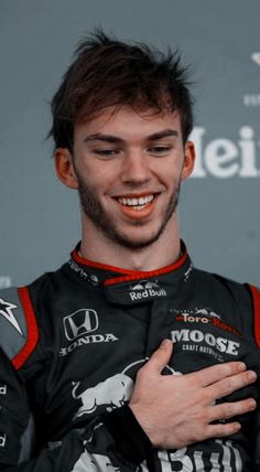 a smiling man with his hands on his chest in front of a sign and microphone