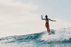 a woman riding a wave on top of a surfboard in the ocean with her arms out