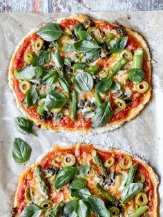 two pizzas with basil leaves and olives on top