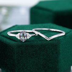 an engagement ring sitting on top of a green velvet box with two diamonds in it