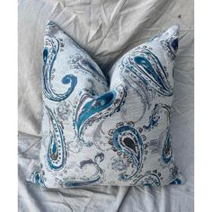 a blue and white pillow sitting on top of a bed next to a gray sheet