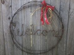 a metal sign that says welcome hanging on a wooden fence with a red ribbon around it