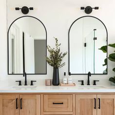 two mirrors are on the wall above double sinks in a bathroom with wood cabinets and black faucets