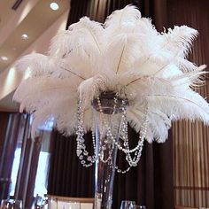 a vase with some feathers in it on a table next to wine glasses and silverware