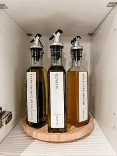 three bottles of liquid sitting on top of a wooden tray in a cabinet next to each other