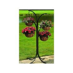 three hanging flower baskets with flowers in them on a pole near the grass and water