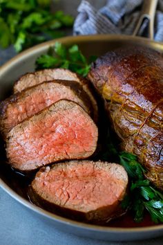 some meat is sitting in a bowl with greens on the side and another piece of meat next to it