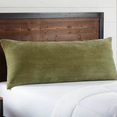 a green pillow on top of a bed next to a night stand with a wooden headboard