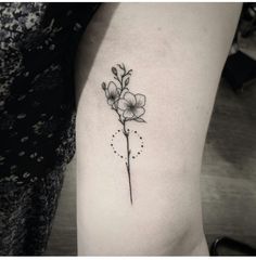 a small flower tattoo on the left side of the arm, with tiny dots around it