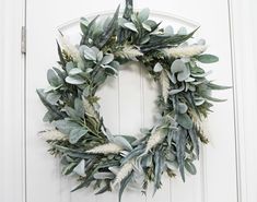 a wreath hanging on the front door with white flowers and green leaves around it's edges