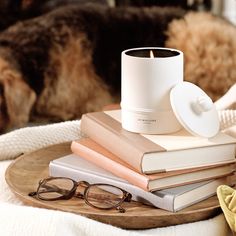 a stack of books sitting on top of a wooden table next to glasses and a candle