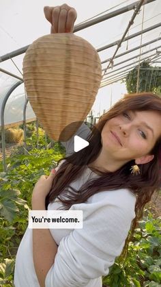 a woman standing in a greenhouse holding up a large object with the caption you're welcome