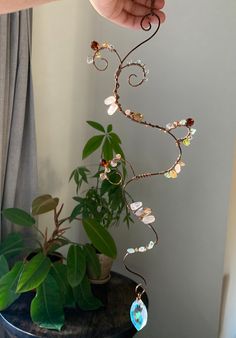 a hand holding a wire sculpture with flowers and leaves on it next to a potted plant