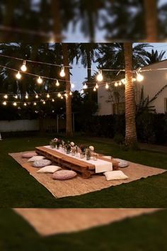 an outdoor picnic with lights strung over it and pillows on the ground, in front of palm trees