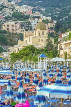 many blue and white umbrellas are on the beach in front of some buildings with hills in the background