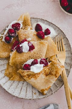 crepes topped with whipped cream and raspberries on a plate next to a fork