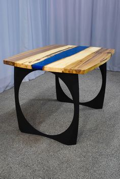 a table made out of wood and metal with a blue strip on the top, sitting in front of a curtain