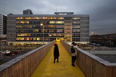 two people walking across a yellow walkway in front of a building