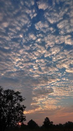 the sky is filled with clouds as the sun sets in the distance behind some trees