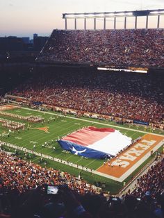 a football stadium filled with lots of people and a giant texas flag on the field