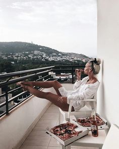 a woman sitting on top of a white chair next to a box of pizzas