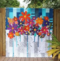 a quilted wall hanging with colorful flowers in the vase on it's side