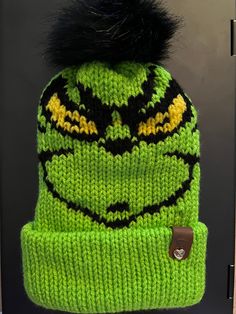 a green and black knitted hat with a fur pom