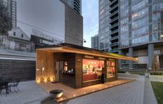 a small wooden building with lights on the outside and in front of some tall buildings