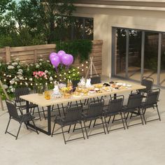 an outdoor dining table with purple balloons and flowers on the outside patio, surrounded by greenery