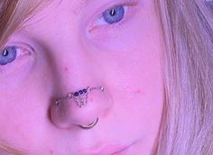 a close up of a person with blue eyes and piercings on their nose,