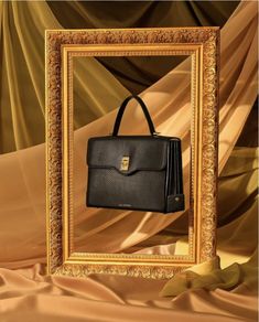 a black purse sitting in front of a gold framed photo frame on a brown cloth