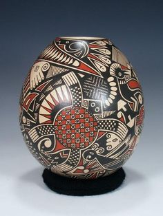 an artisticly decorated vase sitting on top of a black base with red and white designs