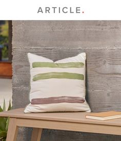 a pillow sitting on top of a wooden bench next to a book and planter