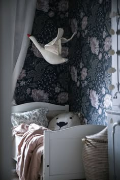 a white bed sitting under a window next to a wall covered in floral wallpaper