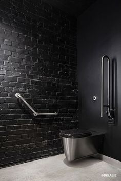 a bathroom with black brick walls and a metal toilet in the middle, along with a hand rail