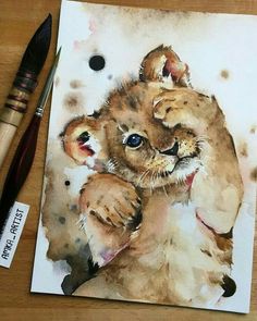 a watercolor painting of a lion cub on paper next to a paintbrush and acrylic brush