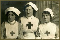 three women in nurses'uniforms are posing for a photo with one woman wearing a red cross on her chest