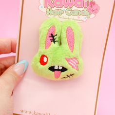 a hand holding a small green stuffed animal on top of a pink card with the words kawai's hair candy written below it