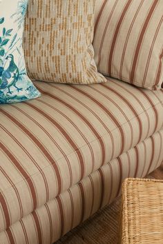 a striped couch with pillows on it and a wicker basket next to the couch