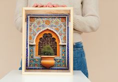 a woman holding up a small photo frame with a potted plant in it