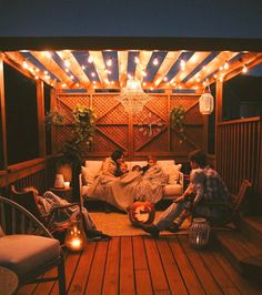 three people sitting on a porch with lights strung over the roof and in the background